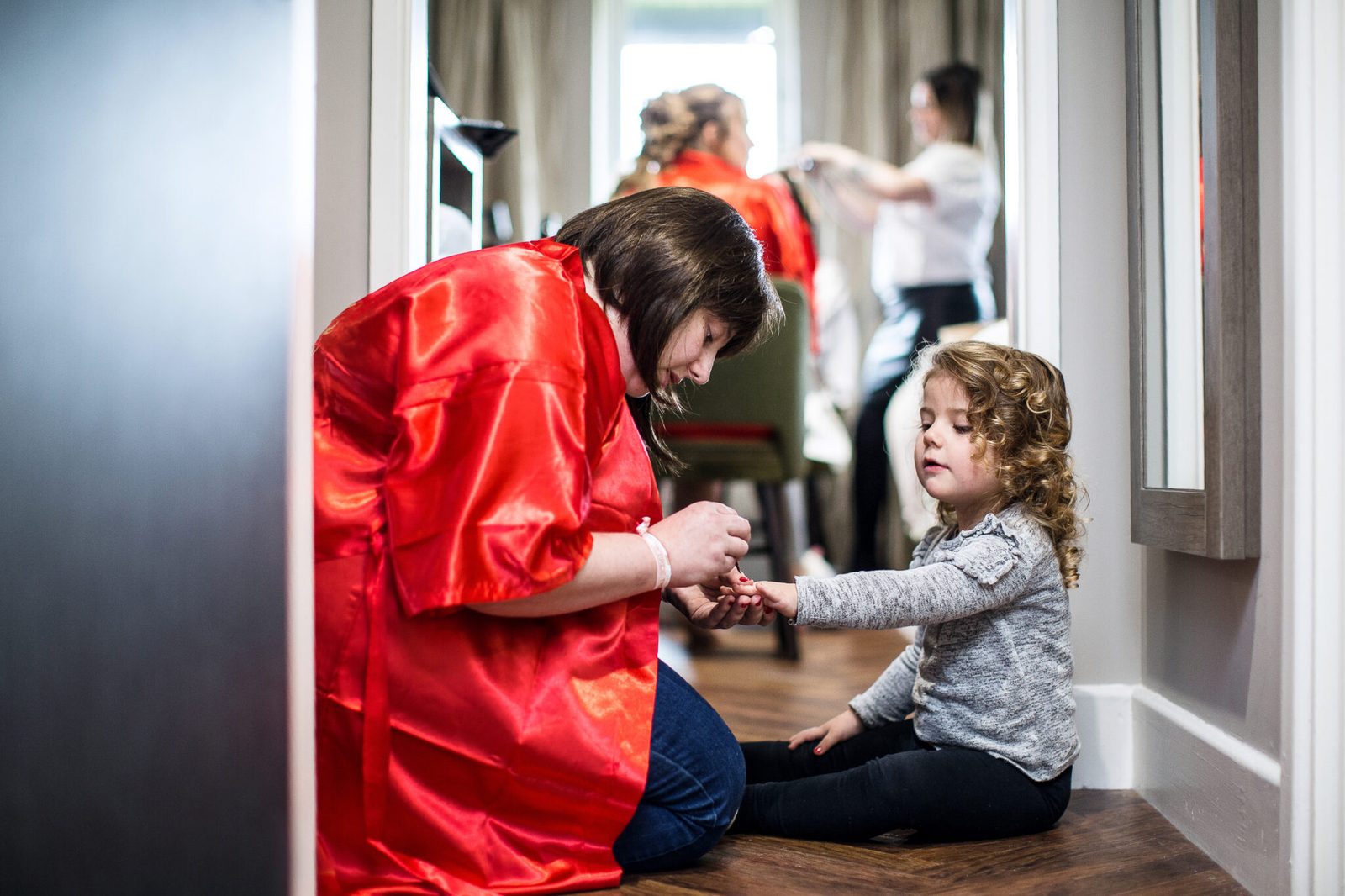 A woman in a red robe helps a little girl with her shoes