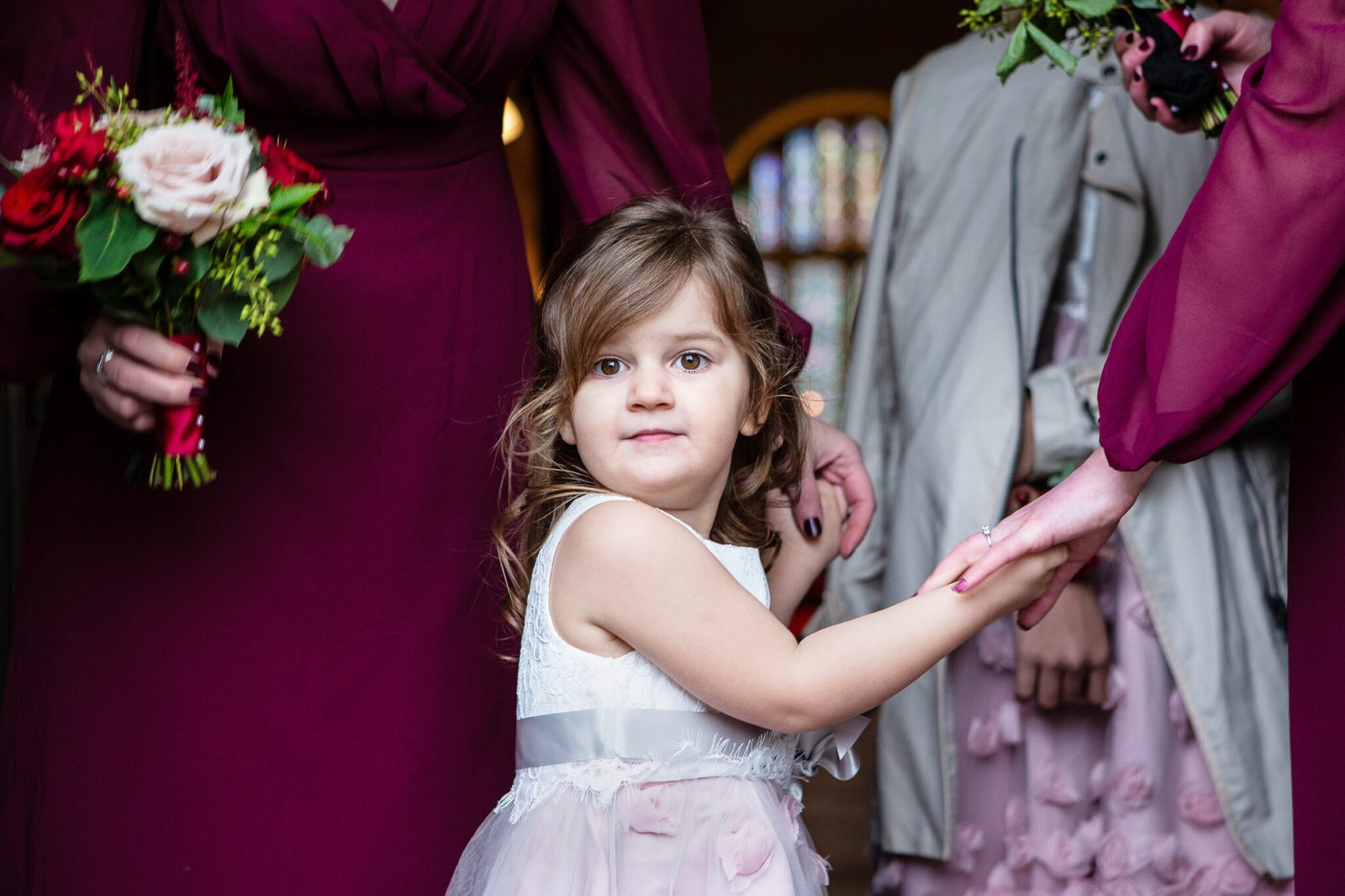 A flower girl holds a grown-up's hand beside a bouquet