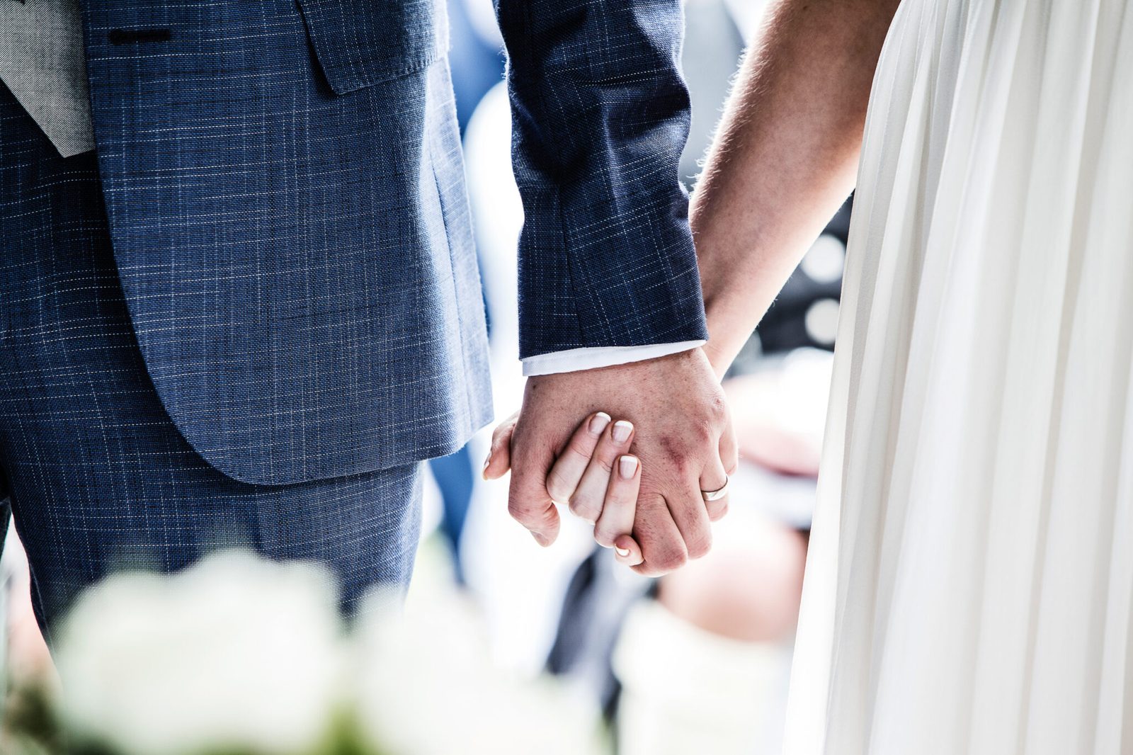 A close view of a couple's hands joined, tweed sleeve against white dress