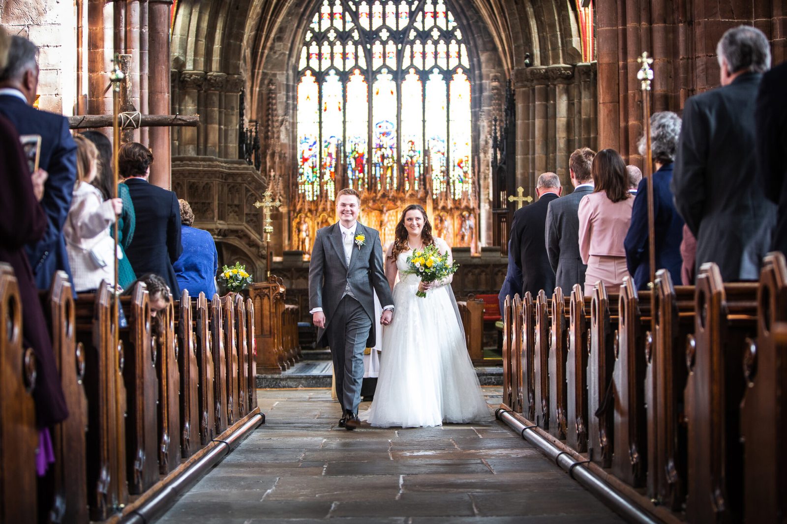 A newly married couple walk back down a church aisle past their guests