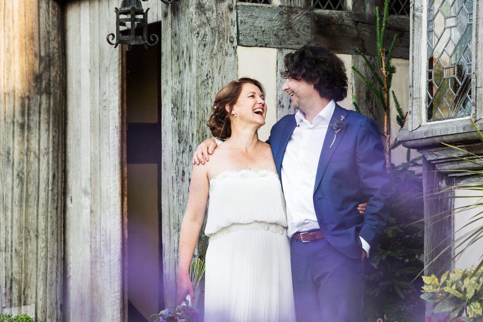 A bride and groom laugh together in a weathered timber doorway