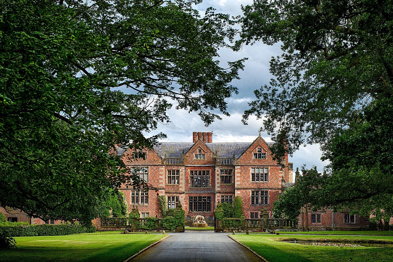 Dorfold Hall's brick Jacobean front framed by trees at the end of the drive
