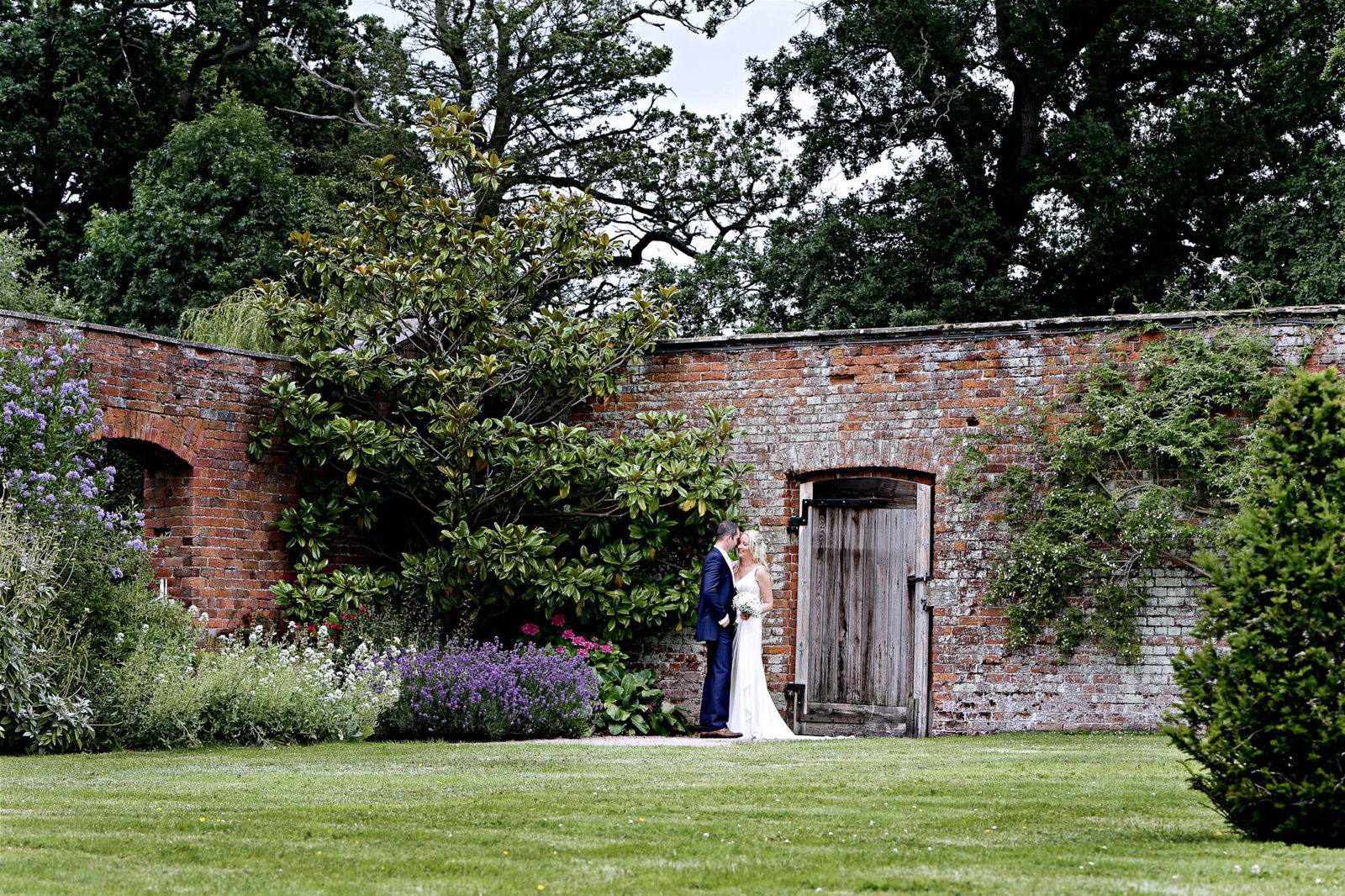 A couple stand by an old wooden door in a walled garden