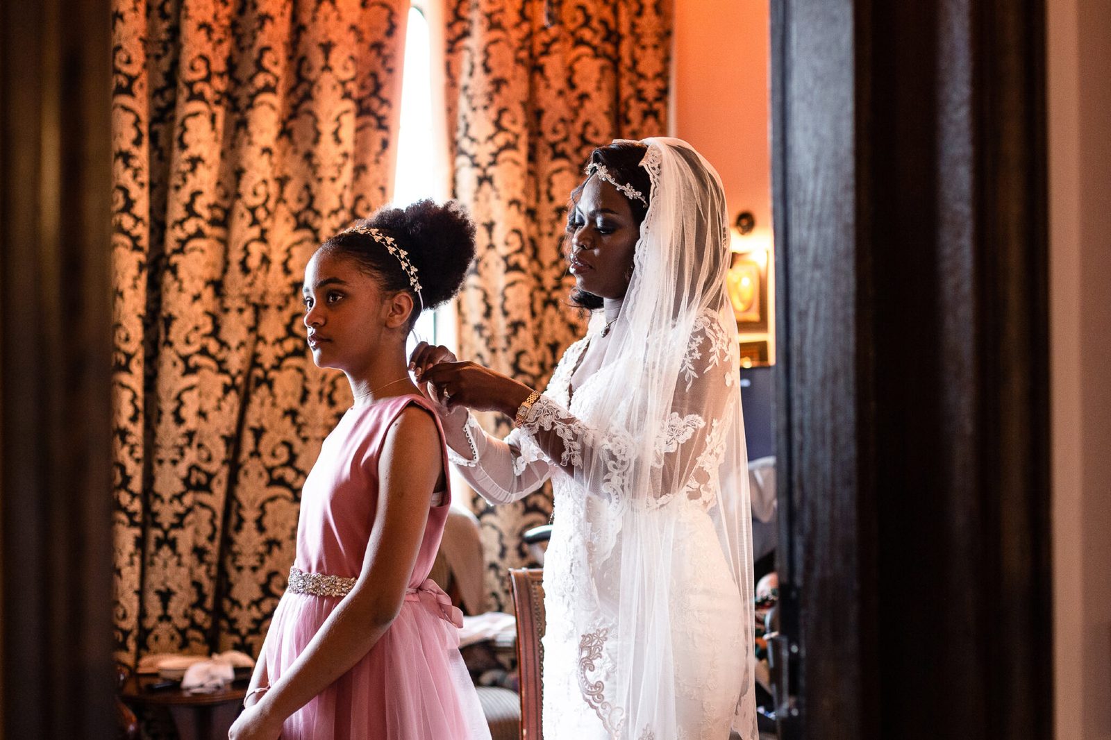 A bridesmaid in pink watches as the bride's veil is arranged