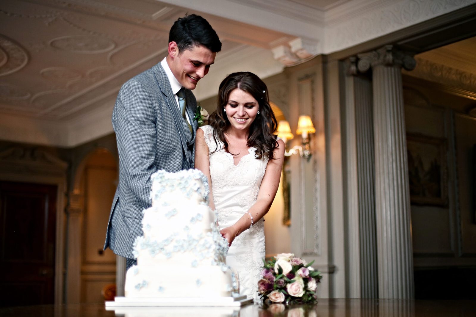A bride and groom cut a tiered white wedding cake