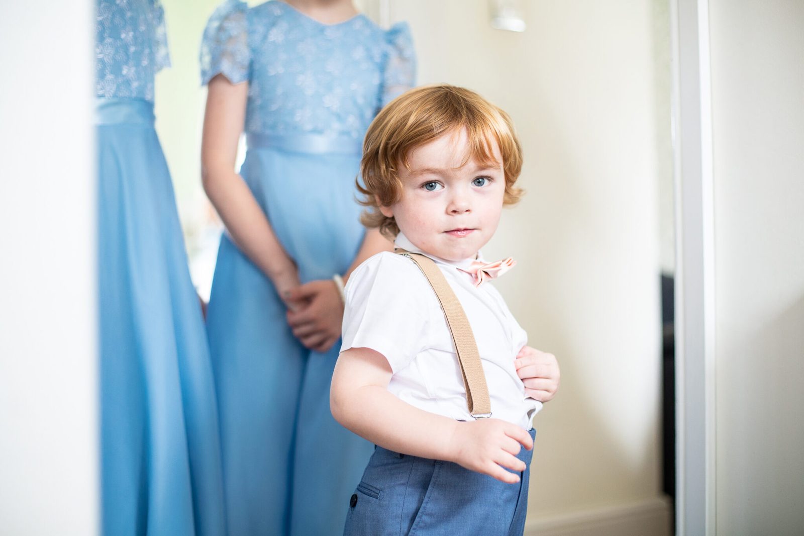 A young page boy in braces stands between bridesmaids in pale blue dresses