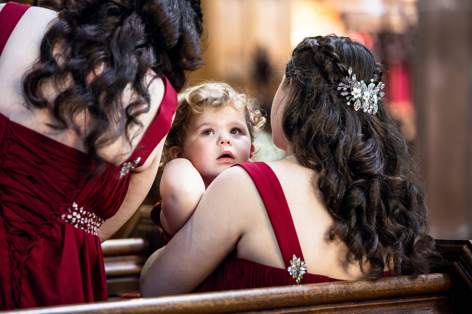 Bridesmaids in burgundy gather round a little girl inside a church