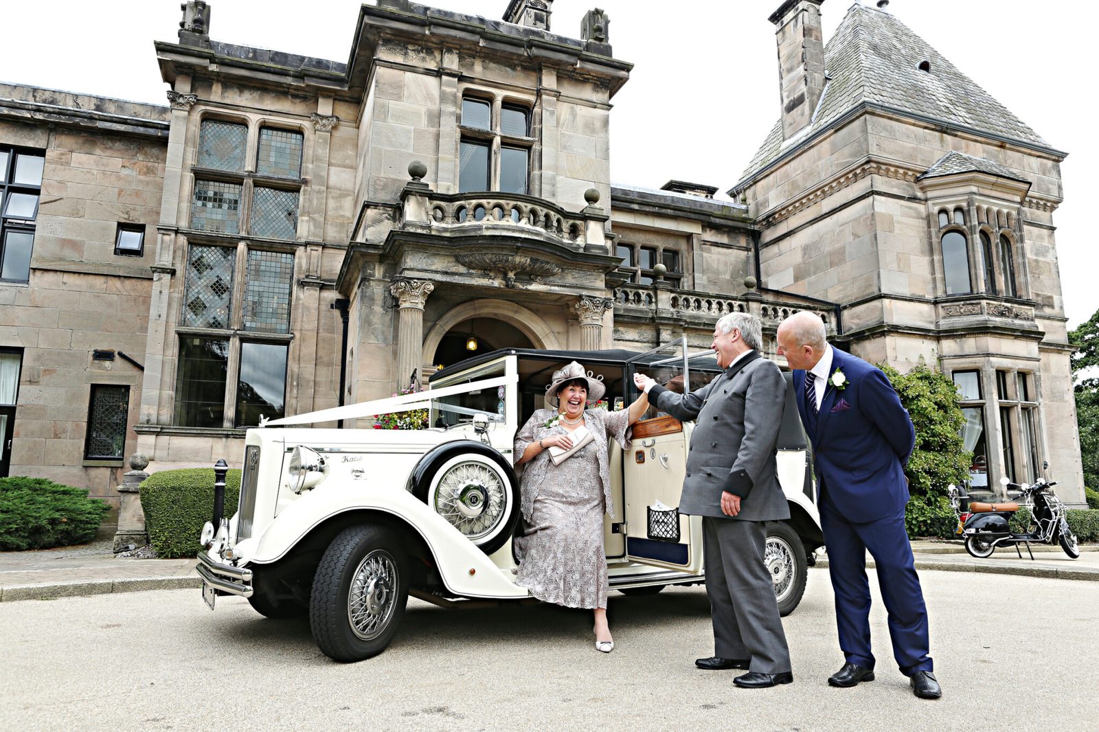 A vintage wedding car outside a stone country house as guests step out