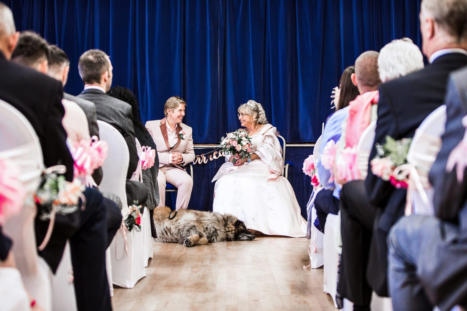 A couple at the front of the ceremony room while a dog lies stretched out in the aisle