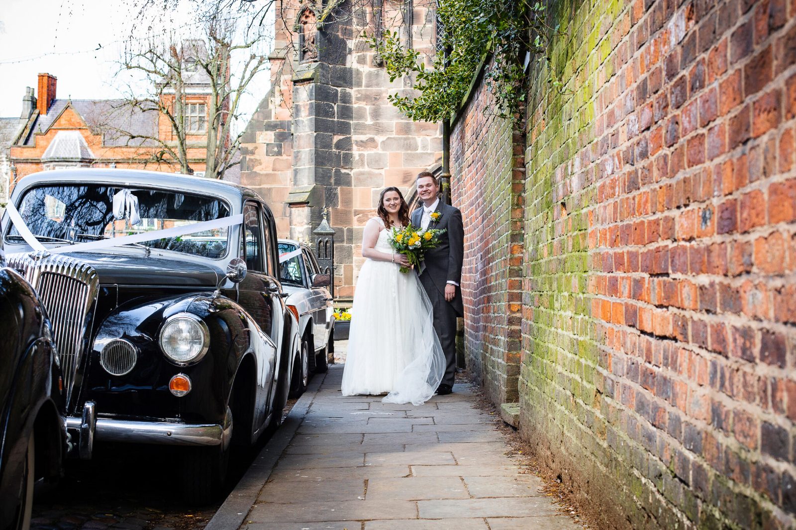 A couple stand by a vintage car in a narrow brick lane
