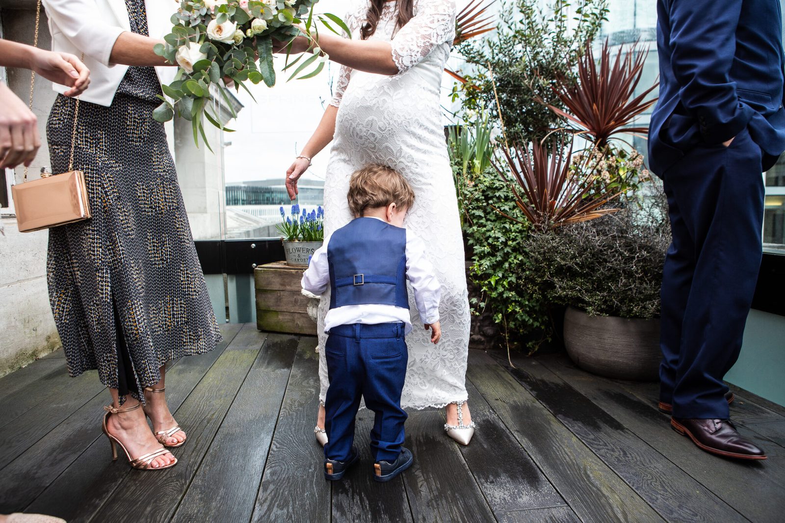 A toddler page boy among guests' legs on a wooden deck