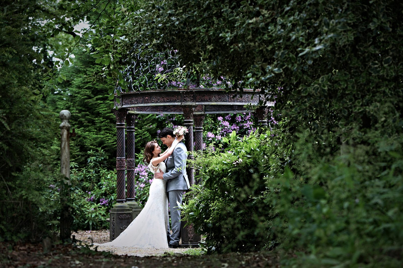 A couple kiss inside a garden gazebo surrounded by greenery
