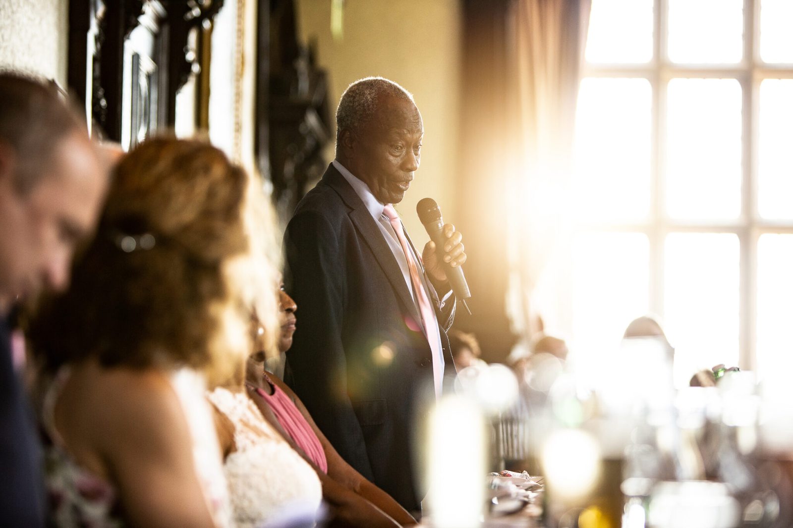 A guest gives a speech into a microphone in warm window light