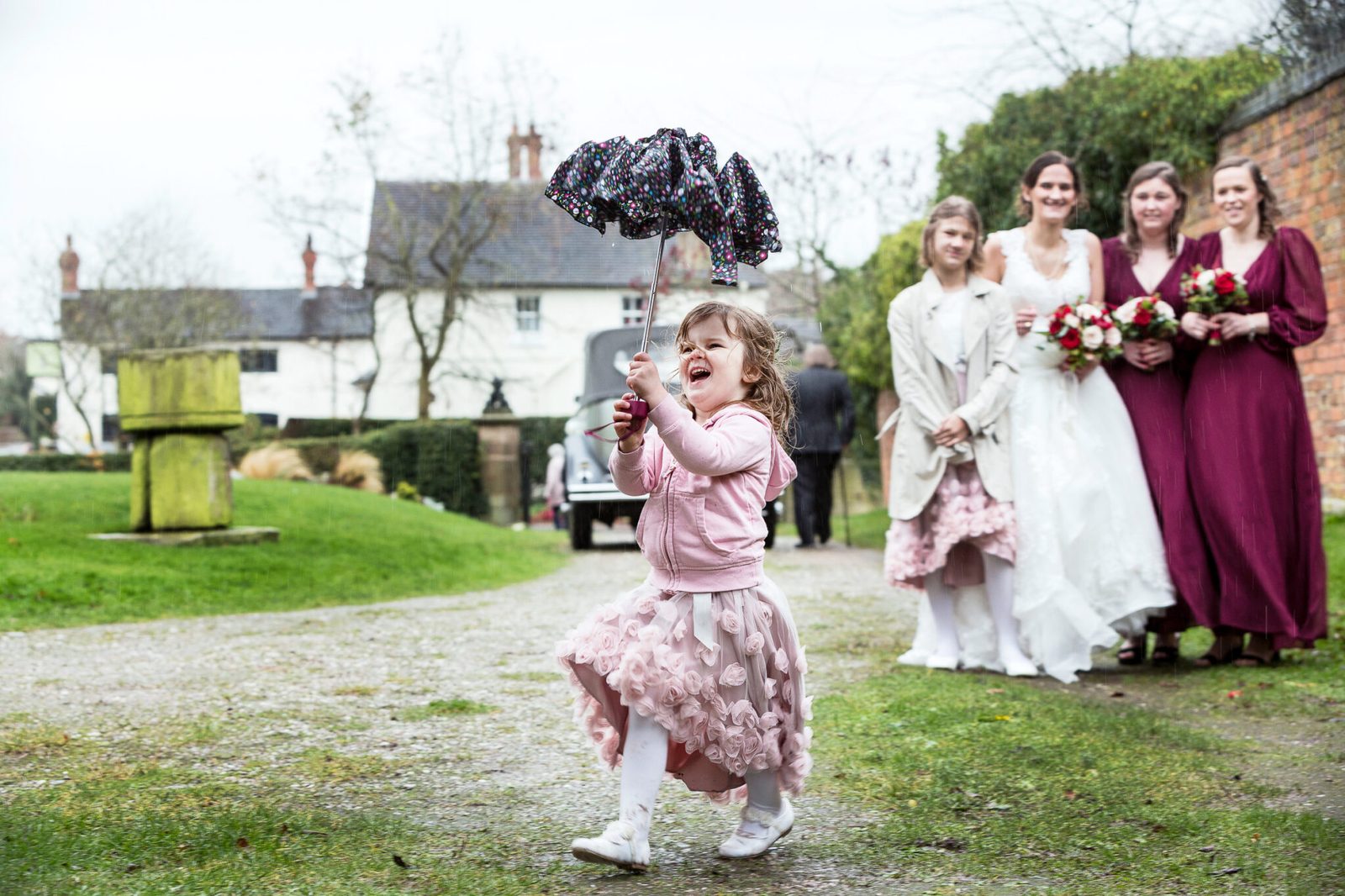 A little girl dances with an umbrella in front of the bridal party