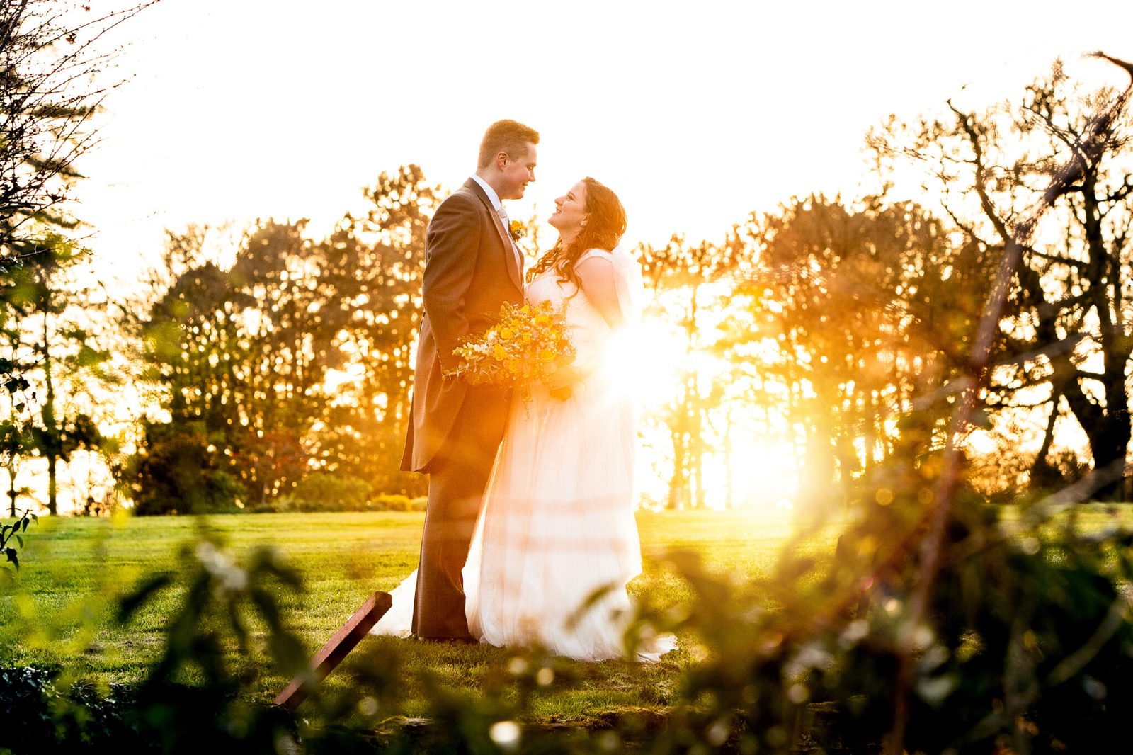 A couple embrace as the sun sets behind trees