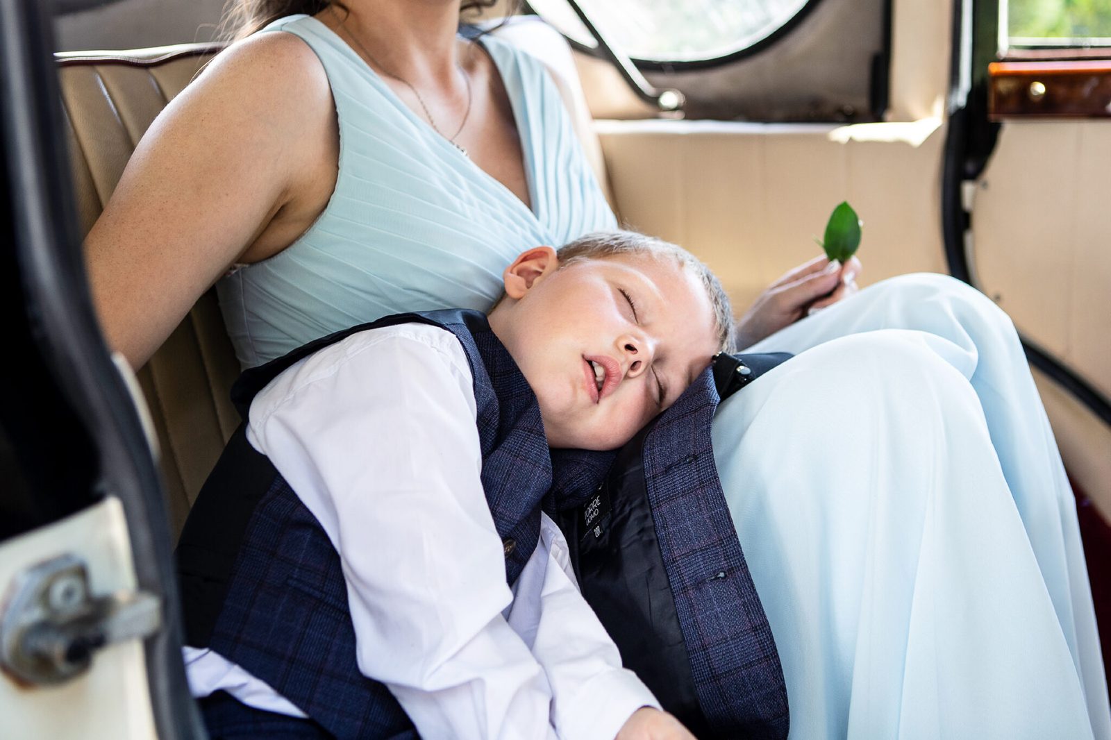 A page boy has fallen asleep across a bridesmaid's lap