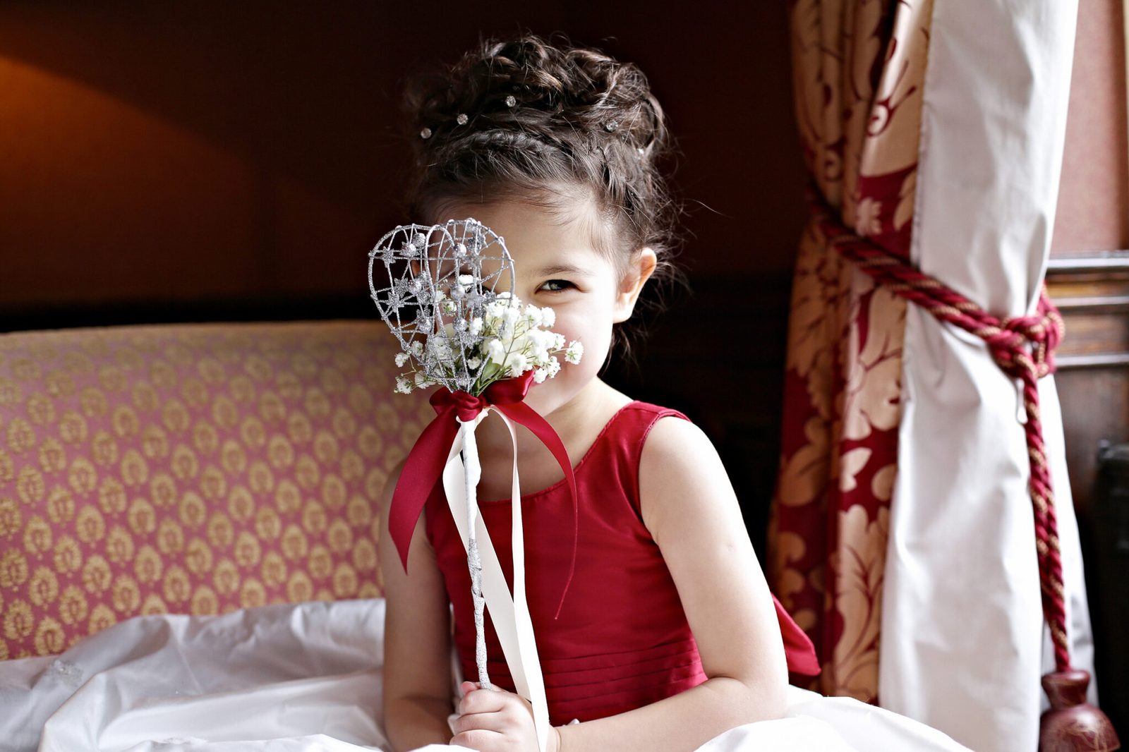 A girl in red peeks out from behind a flower wand