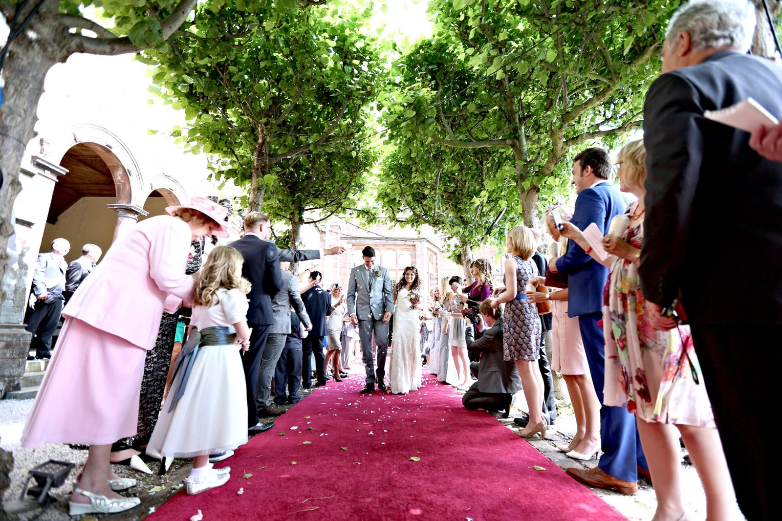 Guests line a red carpet as the couple walk out under the trees