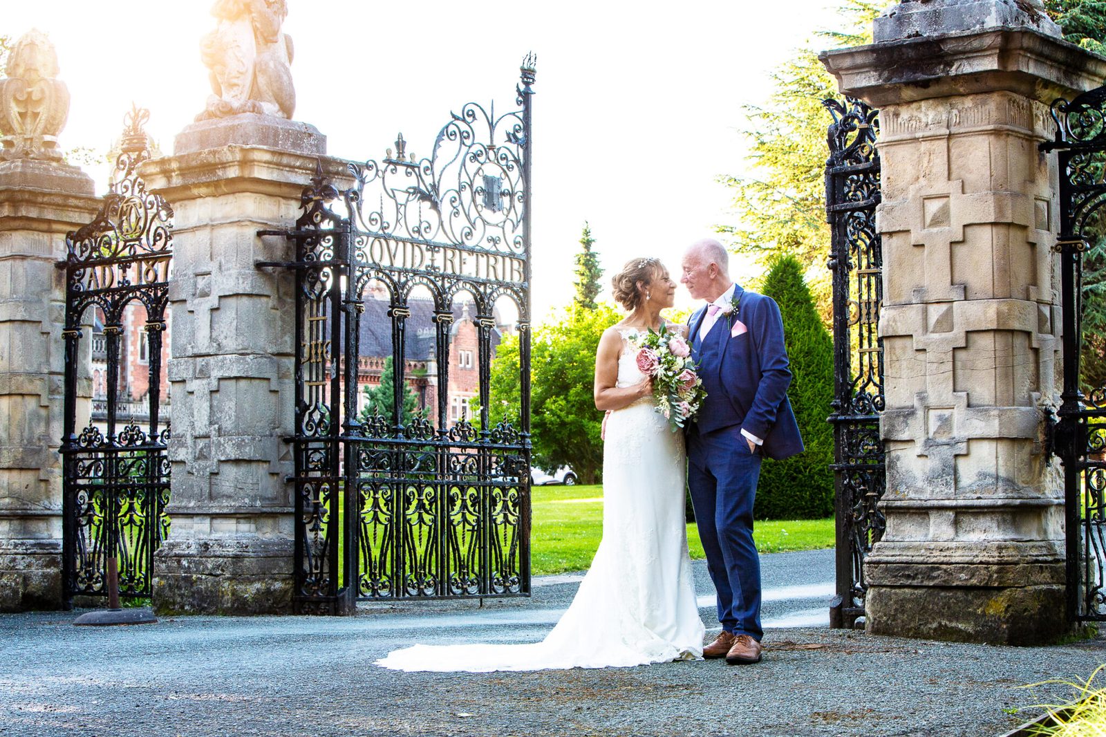 A couple stand beneath ornate iron gates and stone pillars