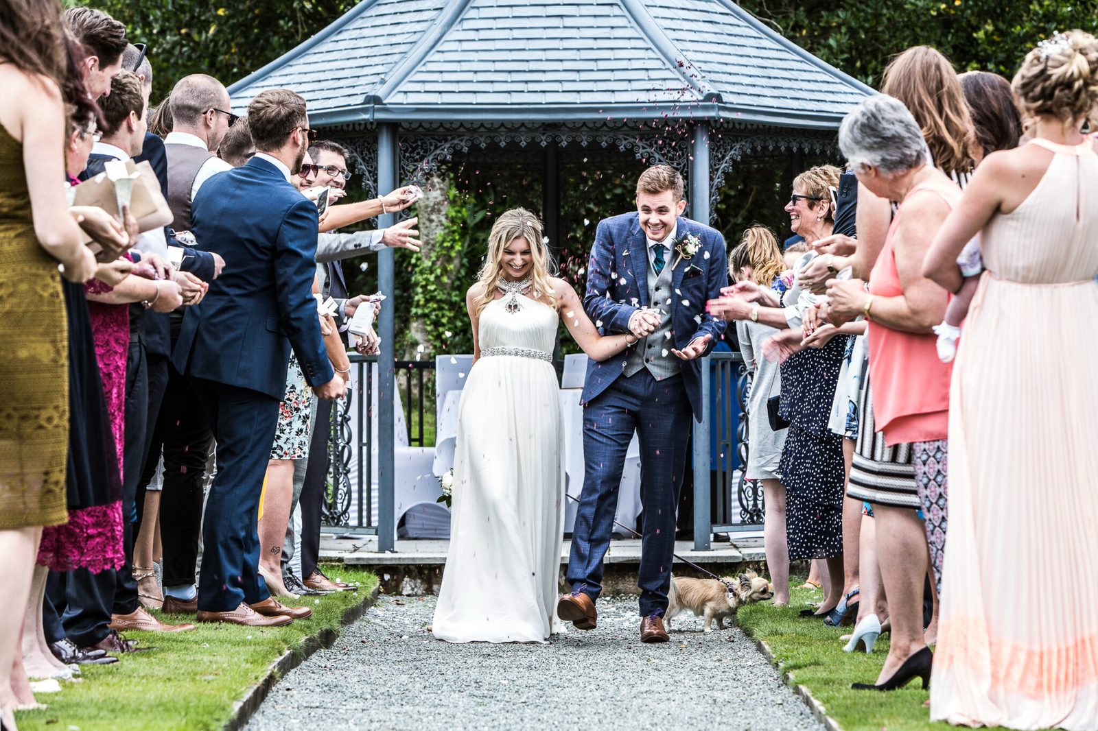 Guests throw confetti as the couple walk from a garden gazebo