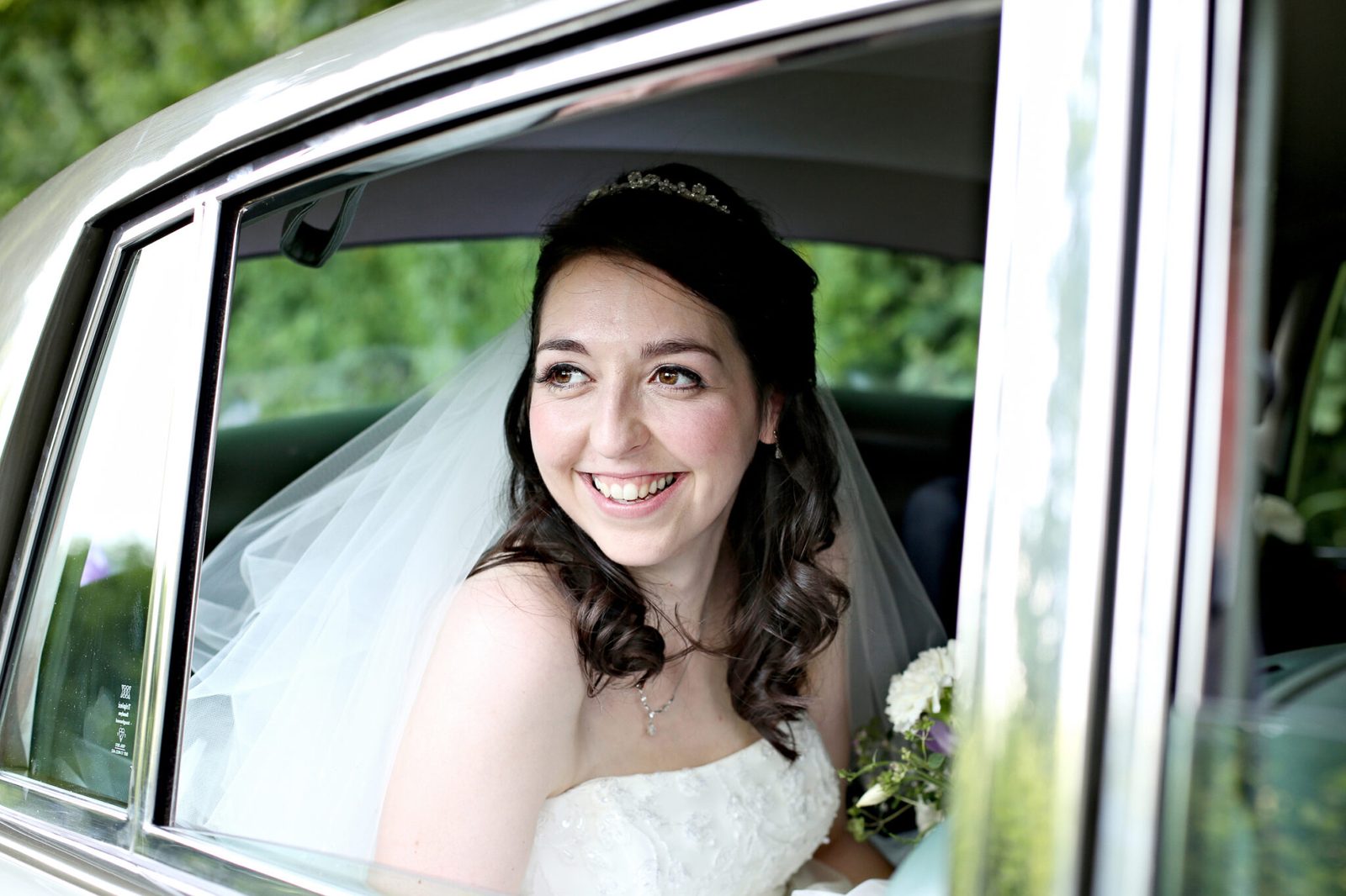 A bride smiles through the window of a vintage car