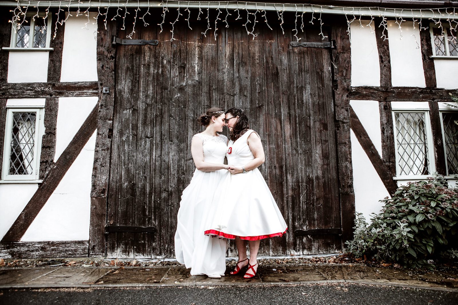 A couple share a kiss by the barn doors of a timber-framed building