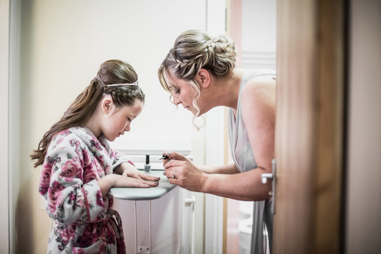 A girl in a dressing gown gets ready at a sink beside a bridesmaid