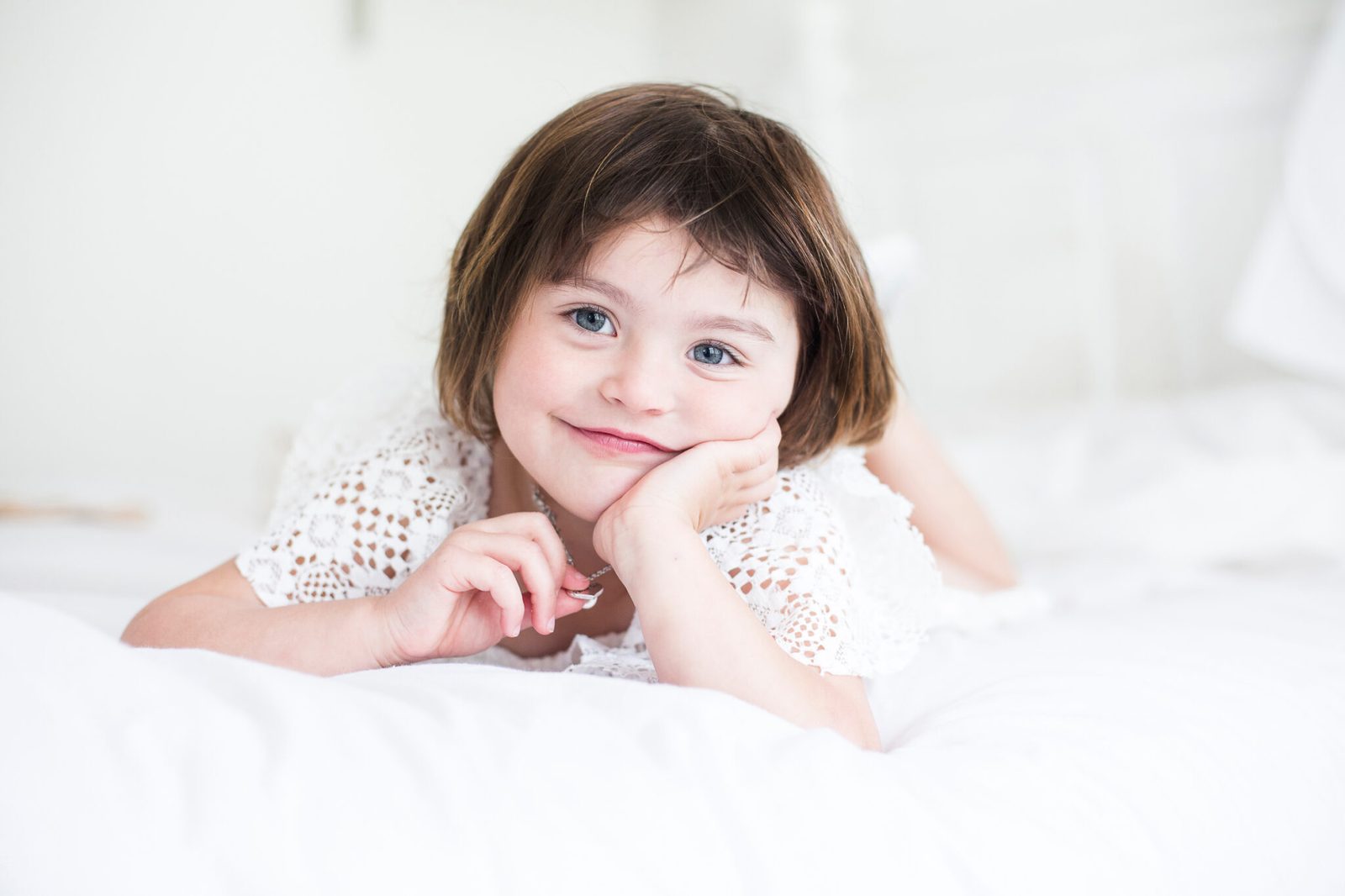 A little girl rests her chin on her hands and grins from the bed