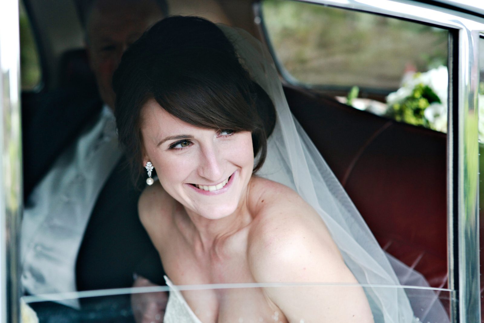 A smiling bride looks out from the window of the wedding car