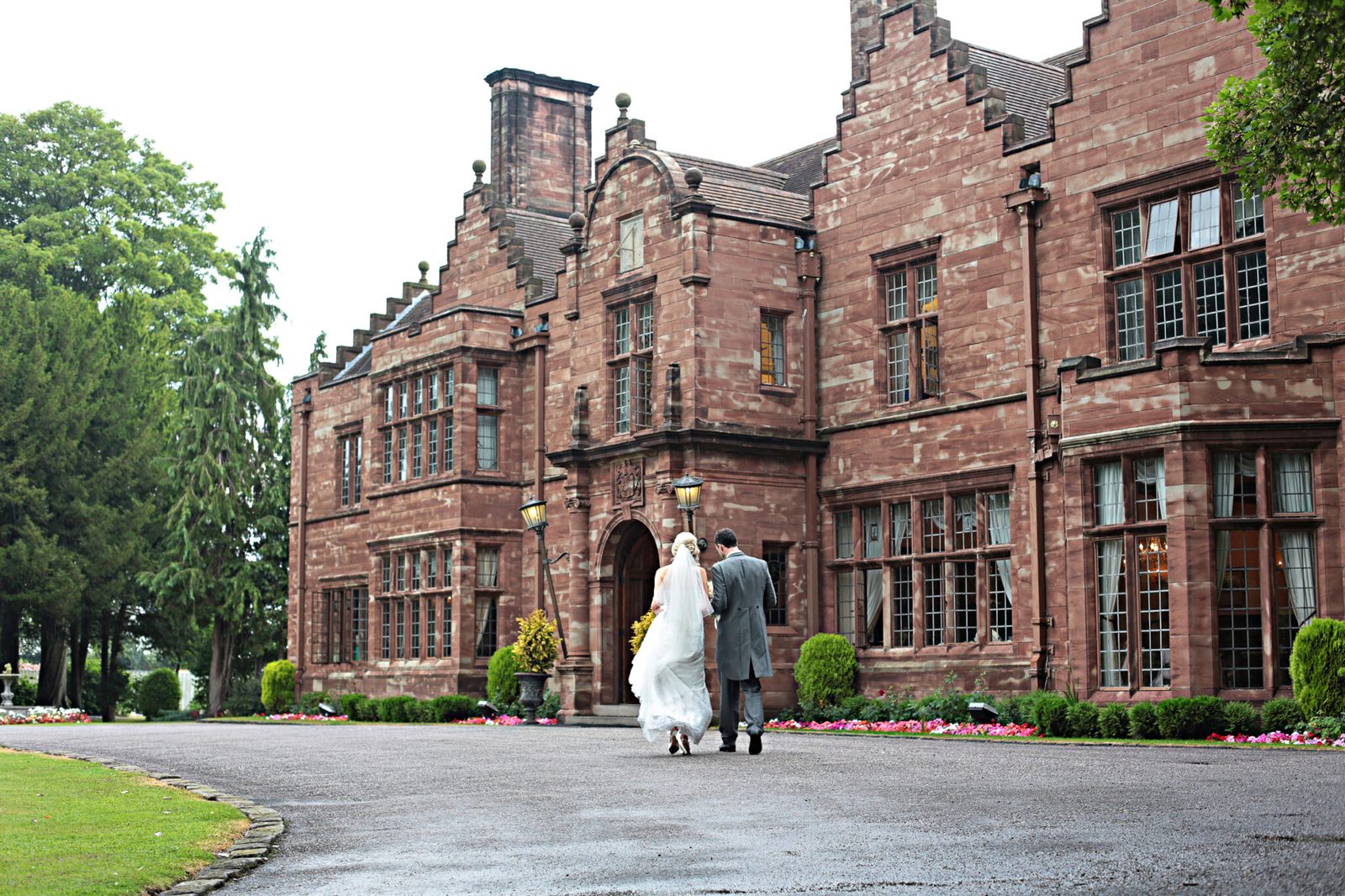 A bride and groom stand small before a red-brick country house