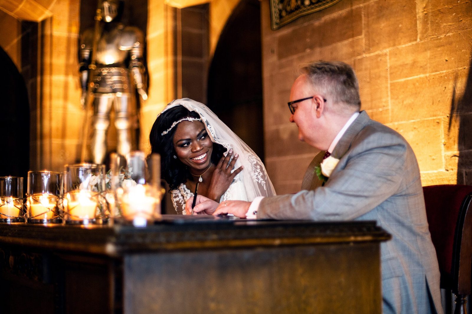 A bride smiles while signing the register by candlelight