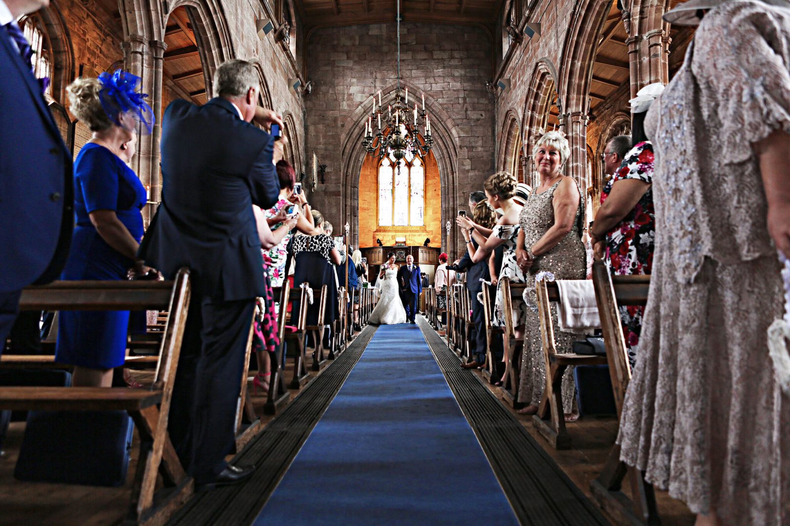 Guests stand in a long church aisle as the bride arrives