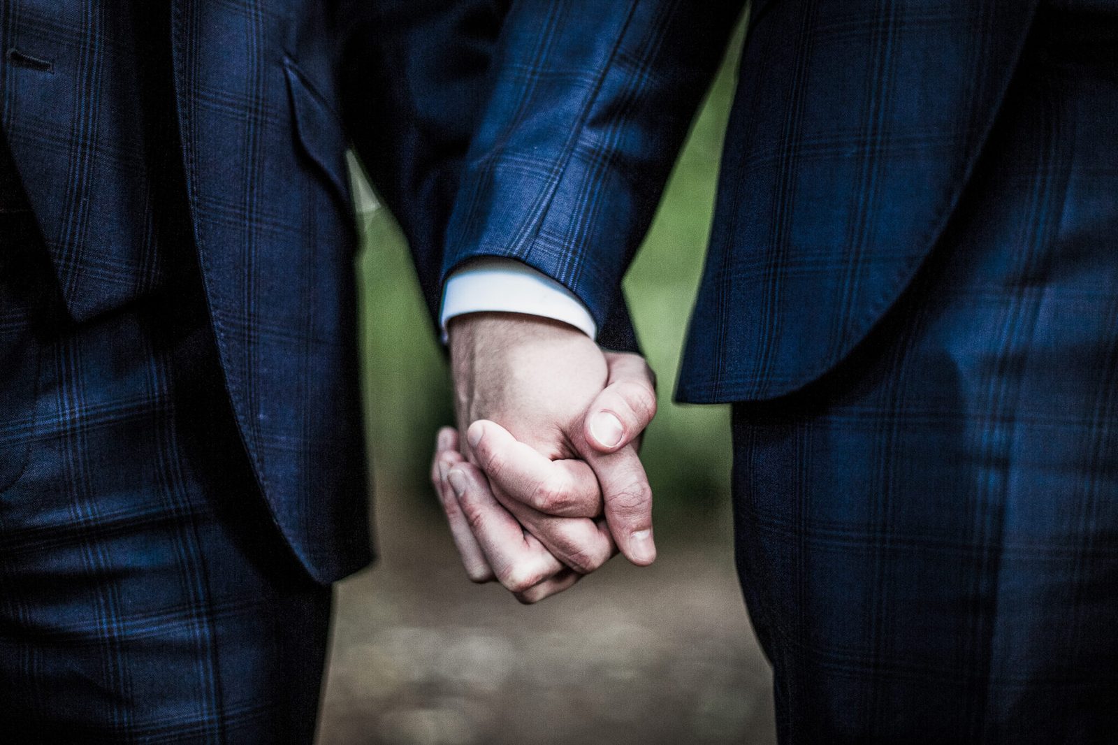 Two grooms' hands clasped together, navy suits
